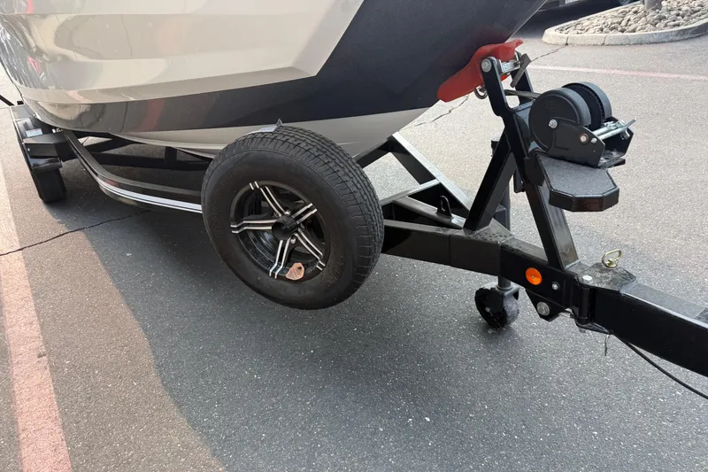 Slide: The Image of 2024 MasterCraft NXT23 boat trailer with black wheel and winch on asphalt. - 9