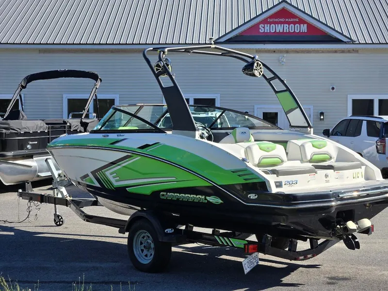 Slide: The Image of 2015 Chaparral 203V boat with green accents parked outside a showroom. - 2