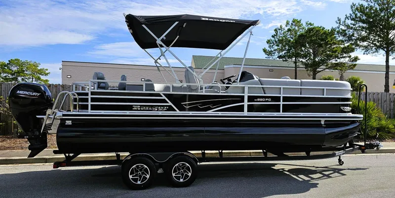 Slide: The Image of 2024 Ranger Reata 220FC pontoon boat with canopy on trailer, parked outdoors. - 0