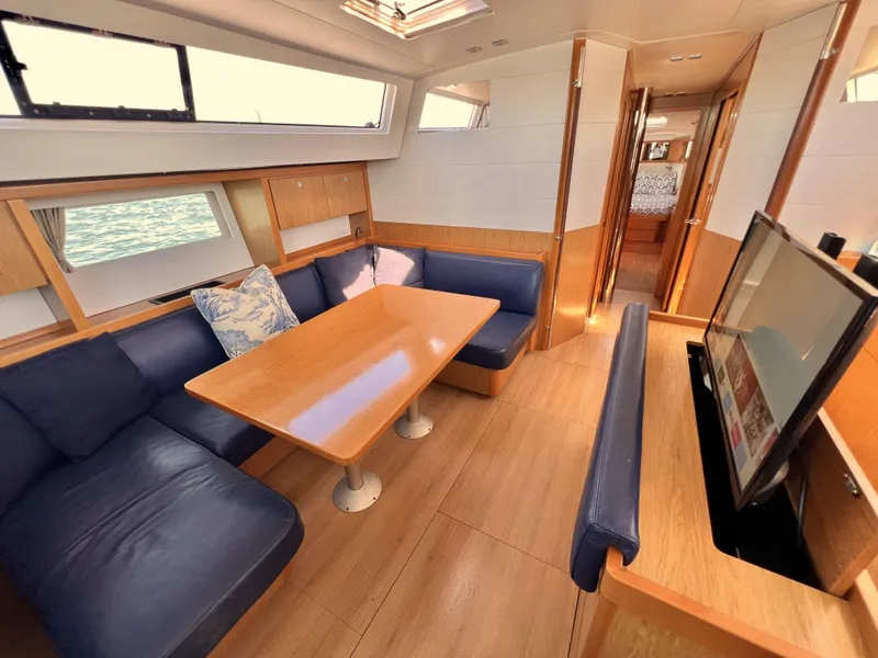 Slide: The Image of 2012 Beneteau Sense 50 yacht interior with blue seating, wooden table, and TV. - 2
