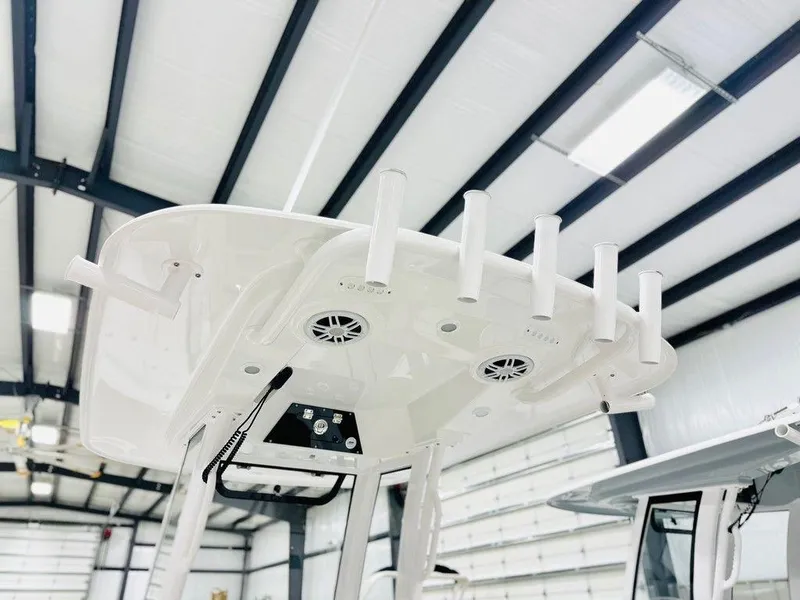 Slide: The Image of 2024 Sportsman MASTERS 247 BAY boat T-top with rod holders and speakers in a warehouse. - 7