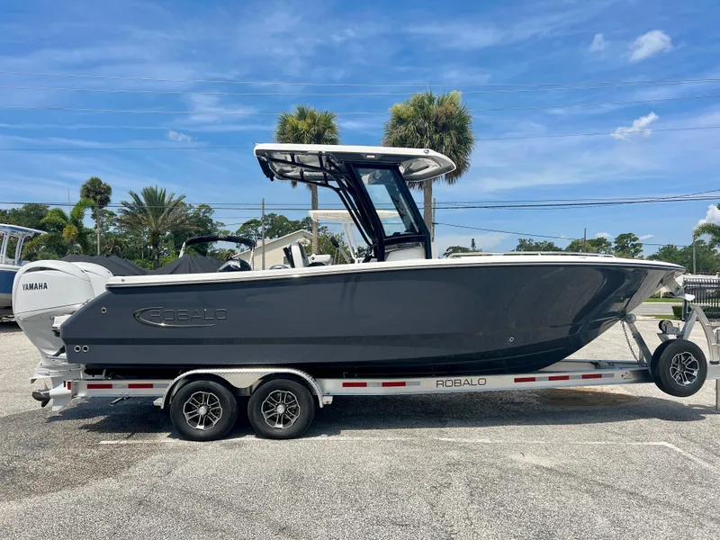 Slide: The Image of 2025 Robalo R250 boat on a trailer with Yamaha engine, parked outdoors. - 0
