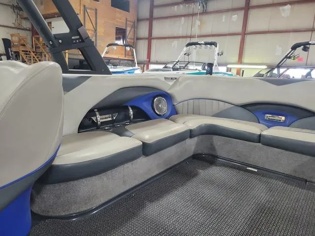 Slide: The Image of 2015 Malibu 247 LSV boat interior with gray and blue seating in a warehouse. - 5