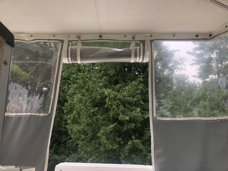 Slide: The Image of Bayliner Ciera 2452 Express 1997 boat interior with clear windows and lush green trees outside. - 14