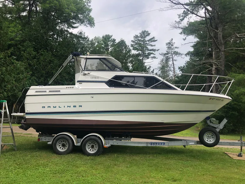 Slide: The Image of 1997 Bayliner Ciera 2452 Express boat on trailer, surrounded by trees. - 1
