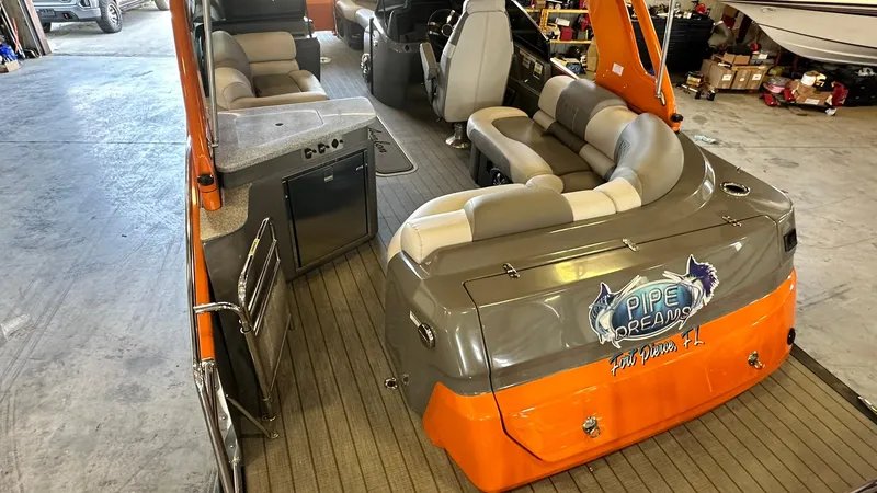 Slide: The Image of 2023 Avalon Excalibur Elite Windshield boat interior with orange and gray seating. - 7