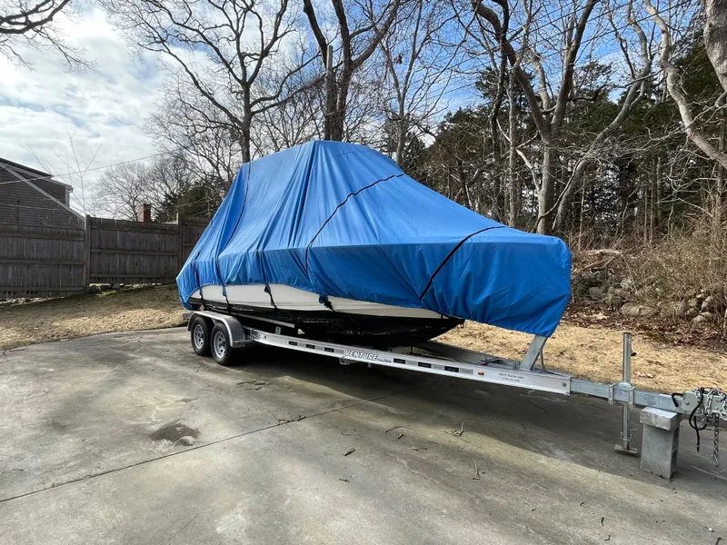 Slide: The Image of 2021 Key West 219 FS boat covered with blue tarp on trailer in wooded area. - 23
