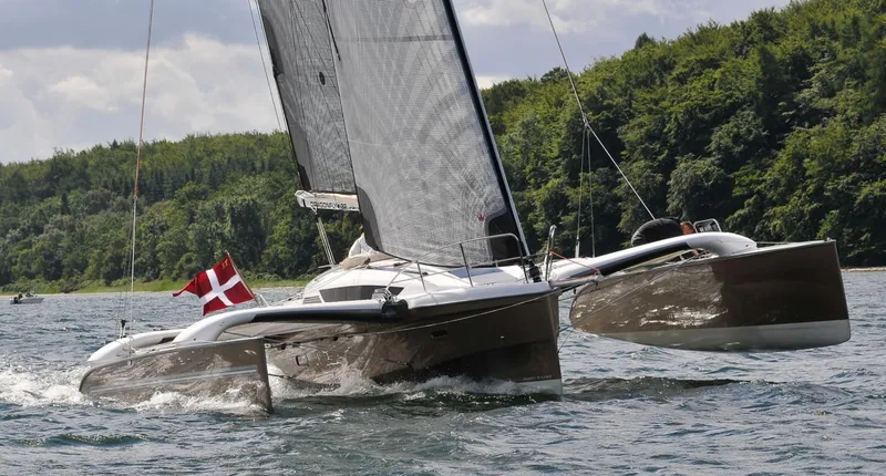 Slide: The Image of Sailing Dragonfly 32 trimaran, 2026 model, on a scenic waterway with lush greenery. - 8