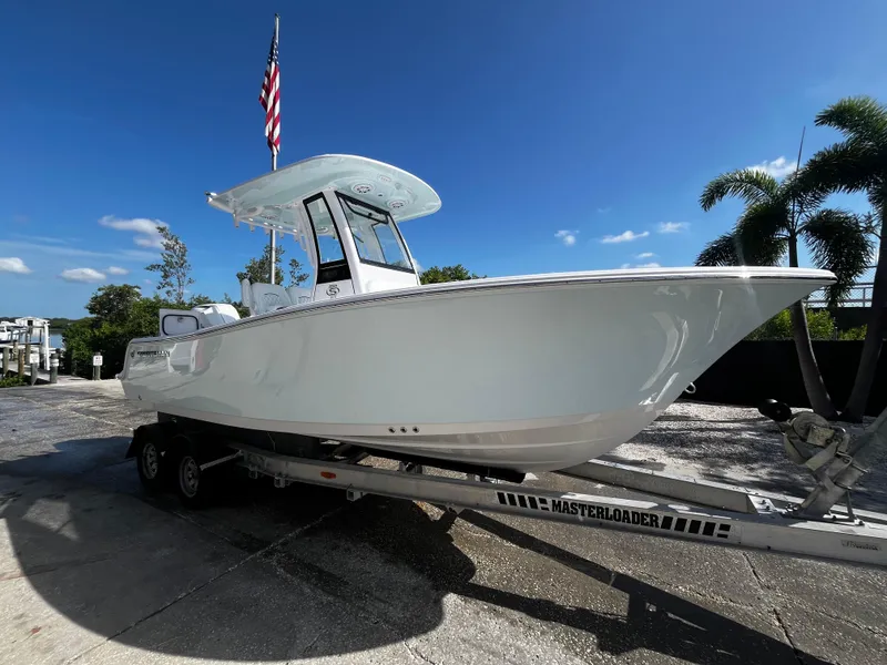 The Image of 2026 Sportsman Open 212 Center Console boat on trailer, with American flag, under clear blue sky. - 0