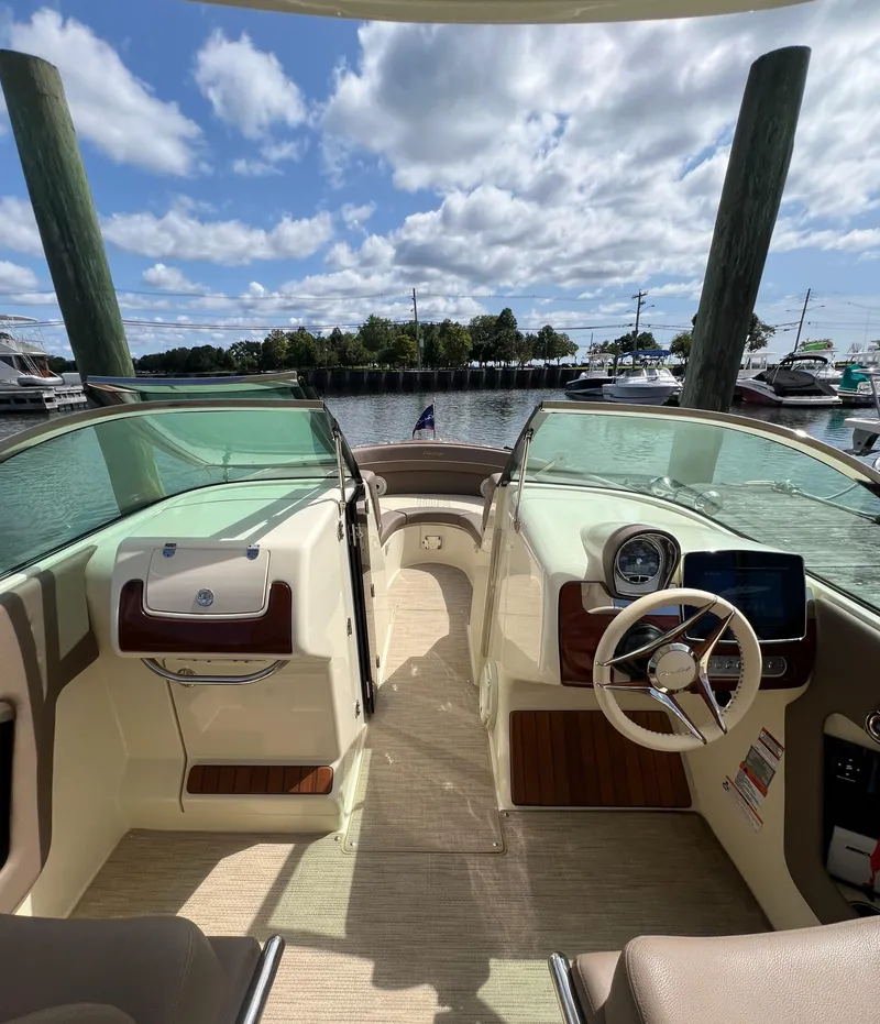 Slide: The Image of 2023 Chris-Craft Launch 28 GT boat interior with steering wheel, dashboard, and waterfront view. - 32