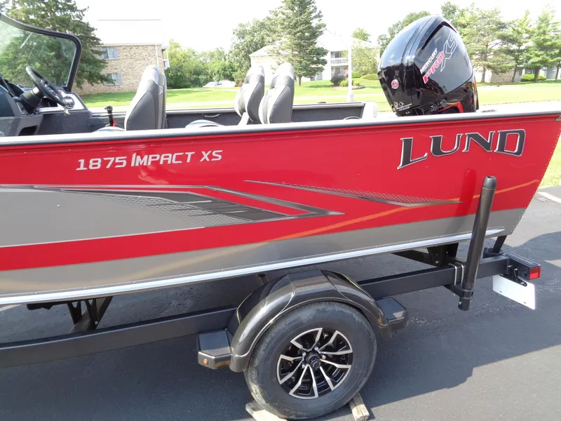 Slide: The Image of 2024 Lund 1875 Impact XS boat, red and gray, on trailer with outboard motor. - 3