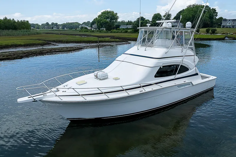Slide: The Image of 2005 Bertram 450 Convertible yacht on calm water, surrounded by lush greenery. - 1