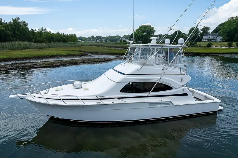 Slide: The Image of 2005 Bertram 450 Convertible yacht on calm water, surrounded by lush greenery. - 11