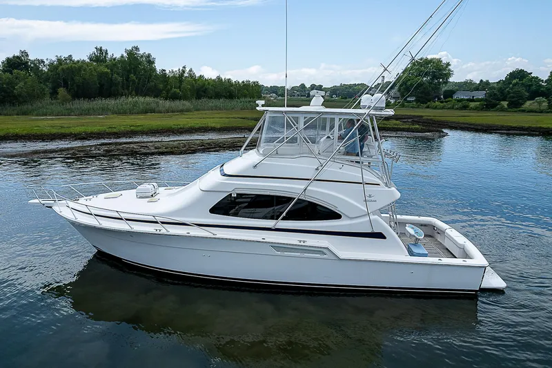 Slide: The Image of 2005 Bertram 450 Convertible yacht on calm water, surrounded by lush greenery. - 12