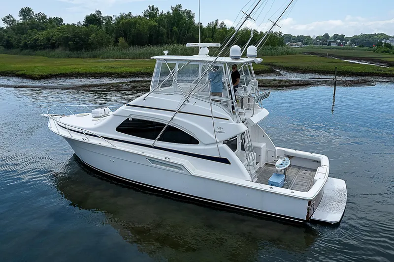 Slide: The Image of 2005 Bertram 450 Convertible yacht on calm water, surrounded by lush greenery. - 13