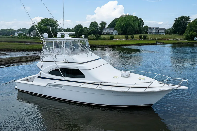 Slide: The Image of 2005 Bertram 450 Convertible yacht on calm water, surrounded by lush greenery. - 5