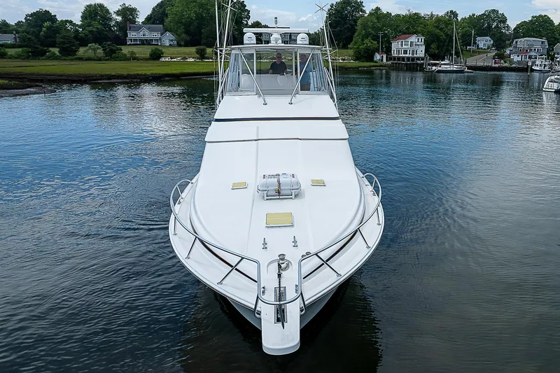 Slide: The Image of 2005 Bertram 450 Convertible yacht on calm water, surrounded by lush greenery and houses. - 9