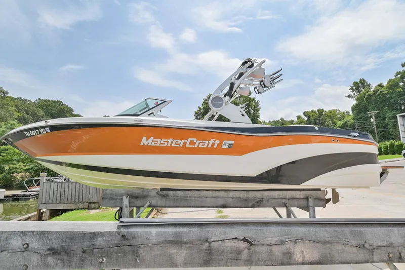 Slide: The Image of 2018 MasterCraft XT23 boat on a lift, orange and white design, outdoors. - 1