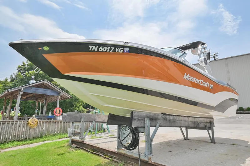 Slide: The Image of 2018 MasterCraft XT23 boat on display, orange and white, parked outdoors. - 2