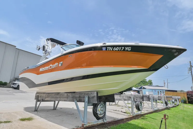 Slide: The Image of 2018 MasterCraft XT23 boat on display, orange and white design, parked outdoors. - 3