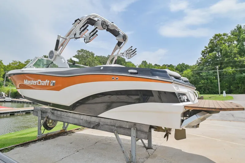 Slide: The Image of 2018 MasterCraft XT23 boat on lift, orange and white design, near a lake. - 6