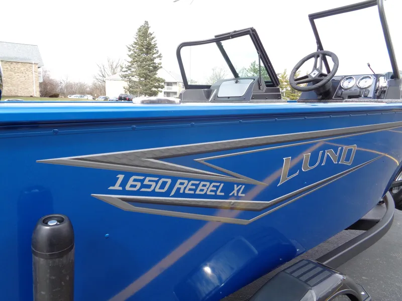 Slide: The Image of 2024 Lund 1650 Rebel XL Sport boat, blue exterior, side view with steering wheel and windshield. - 3