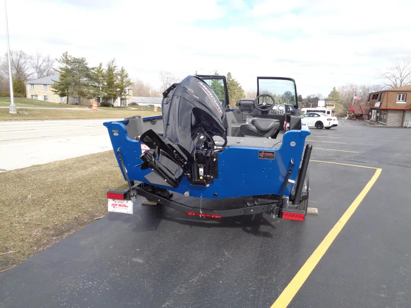 Slide: The Image of 2024 Lund 1650 Rebel XL Sport boat with outboard motor on trailer, parked outdoors. - 4