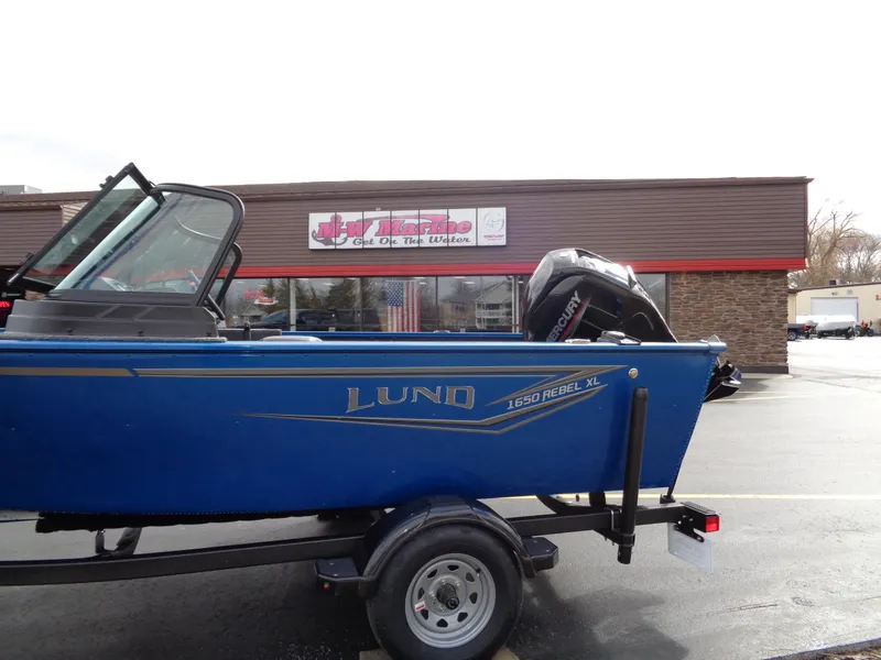 Slide: The Image of 2024 Lund 1650 Rebel XL Sport boat on trailer, parked outside a building. - 6