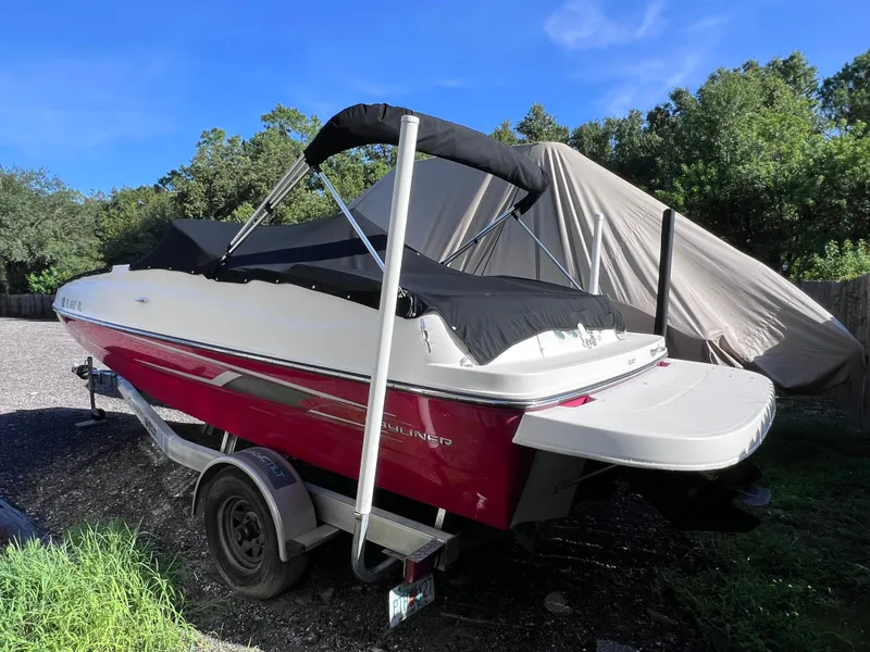 Slide: The Image of 2016 Bayliner 195 Deck Boat with red and white exterior, parked on a trailer. - 4