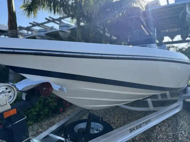 Slide: The Image of 2024 Skeeter SX230 boat on trailer, side view with palm trees in background. - 4