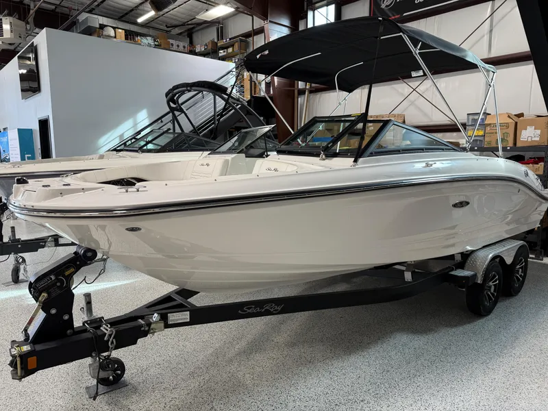 Slide: The Image of 2023 Sea Ray SPX 210 boat in showroom, white exterior, black canopy, on trailer. - 2