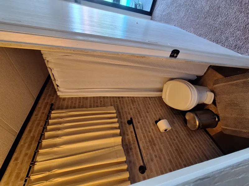 Slide: The Image of 1986 Skipperliner houseboat bathroom with toilet, shower curtain, and window with beige curtains. - 10