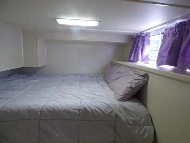 Slide: The Image of Small bedroom in a 2003 Sunstar 16x65 houseboat with purple curtains and a cozy bed. - 6