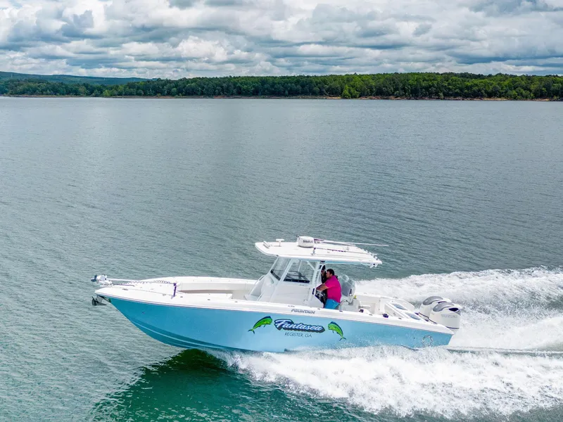 Slide: The Image of 2019 Fountain 34CC boat cruising on a lake with lush green shoreline. - 2