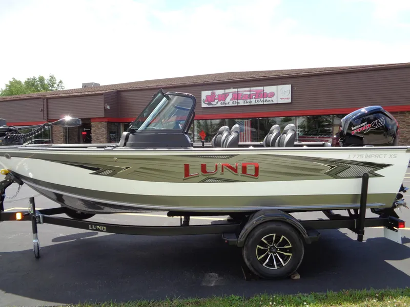 Slide: The Image of 2024 Lund 1775 Impact XS fishing boat on trailer in front of dealership. - 2