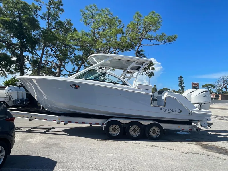 Slide: The Image of 2024 Robalo R317 Dual Console boat on a trailer in a parking lot. - 2