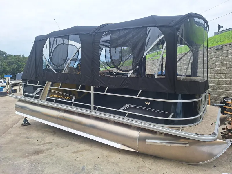 The Image of 2024 Starcraft EX 22 Weekender pontoon boat with black canopy on a concrete surface. - 0