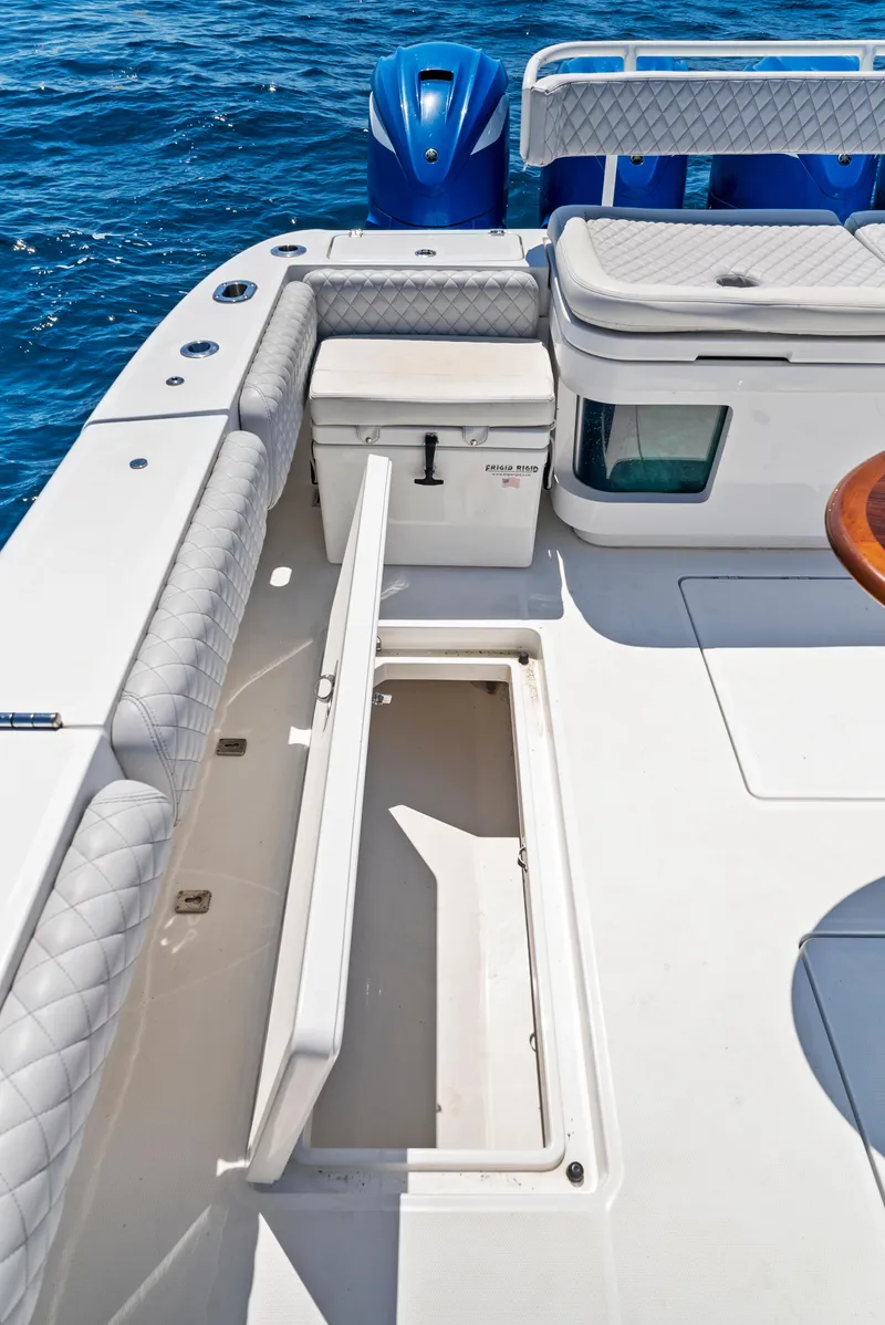 Slide: The Image of 2022 HCB Suenos boat deck with storage compartment open, featuring quilted seating and ocean backdrop. - 34