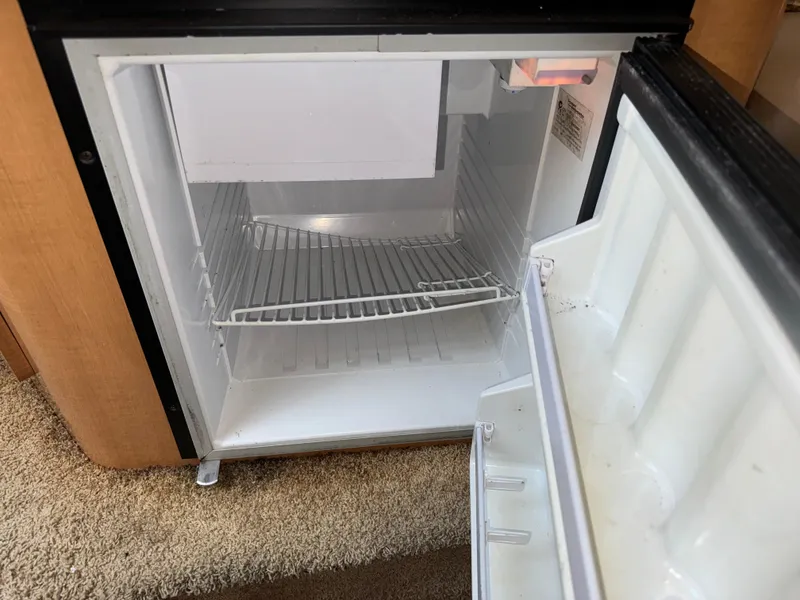 Slide: The Image of Open mini fridge inside 2011 Glastron GS 289 boat, showing empty shelves. - 44