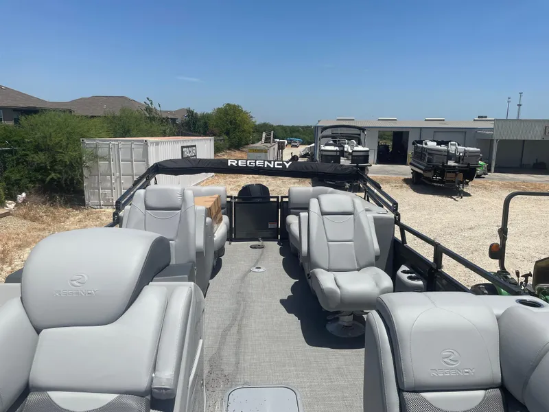Slide: The Image of 2024 Regency 230 DL3 pontoon boat with luxurious seating, parked outdoors under clear skies. - 7