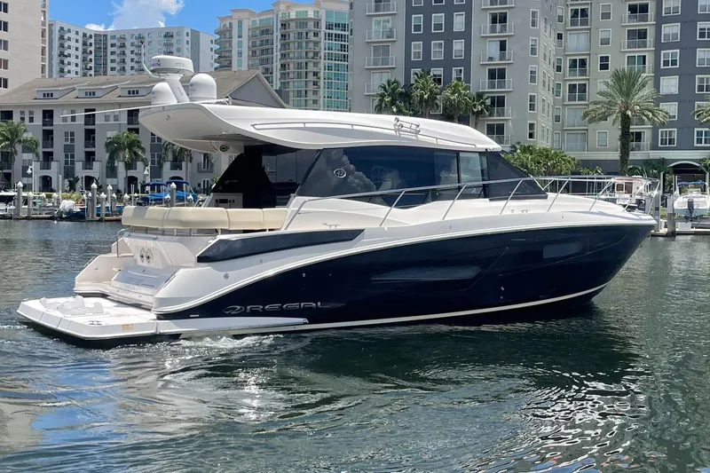 Slide: The Image of 2019 Regal 42 Grande Coupe yacht docked in a marina with modern buildings in the background. - 2