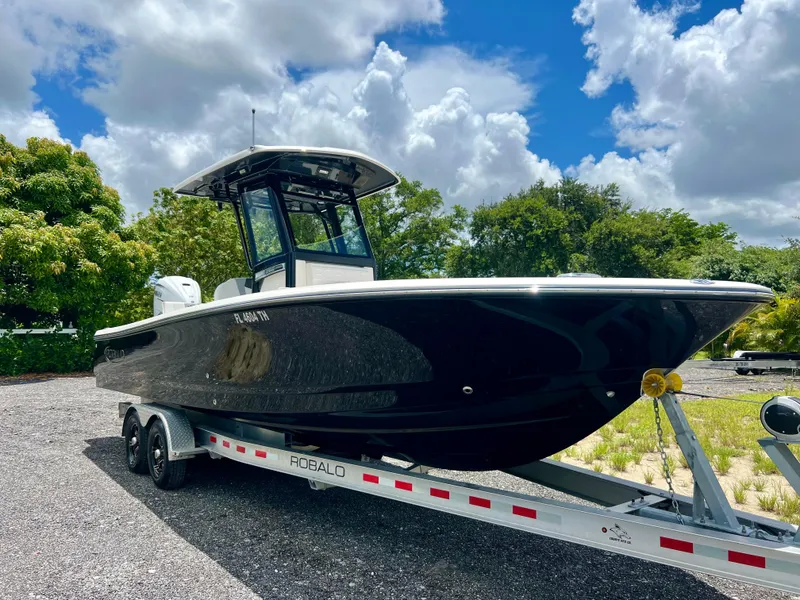 Slide: The Image of 2022 Robalo 266 Cayman boat on a trailer under a partly cloudy sky. - 2