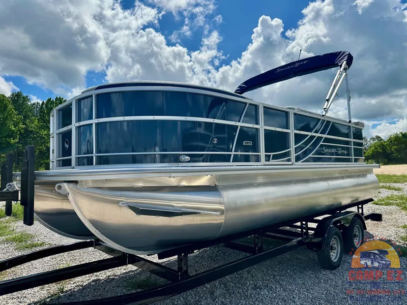 Slide: The Image of 2025 South Bay 220CR LE pontoon boat on a trailer under a partly cloudy sky. - 2