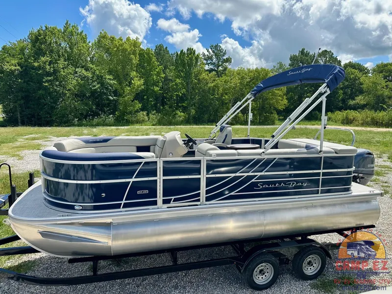 Slide: The Image of 2025 South Bay 220CR LE pontoon boat on a trailer, blue and silver, outdoor setting. - 4