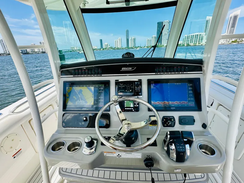 Slide: The Image of 2016 Boston Whaler 350 Outrage helm with navigation screens, steering wheel, and city skyline view. - 11