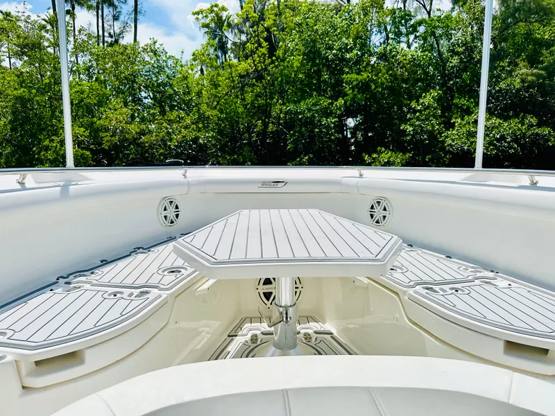 Slide: The Image of 2016 Boston Whaler 350 Outrage boat interior with seating and table, surrounded by greenery. - 6