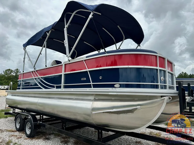 Slide: The Image of 2025 South Bay 224CR LE pontoon boat with blue and red exterior on a trailer. - 2