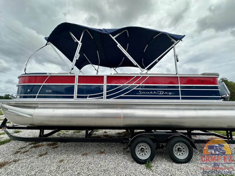 Slide: The Image of 2025 South Bay 224CR LE pontoon boat with blue and red exterior on a trailer. - 4