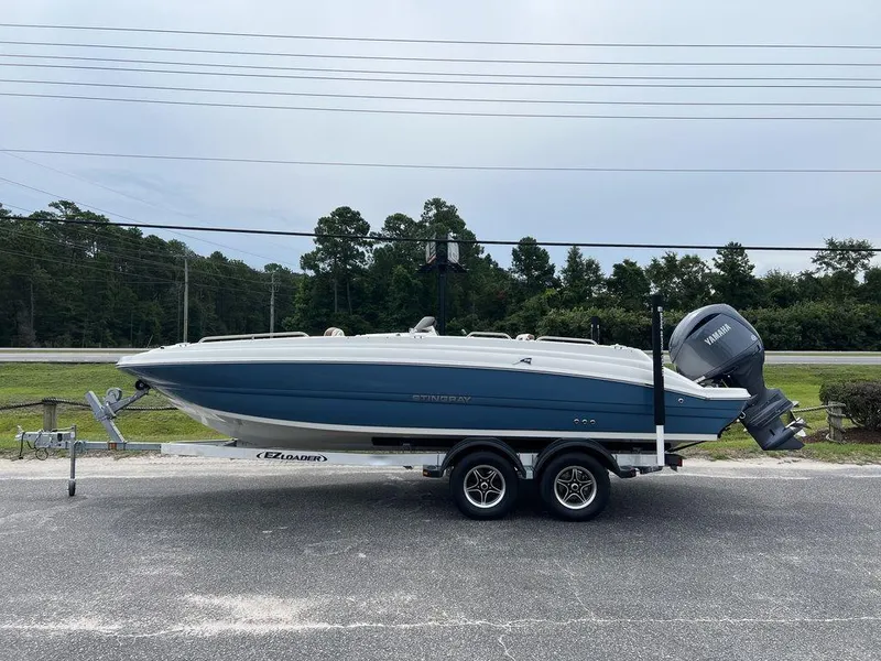 The Image of 2024 Stingray 212SC boat on trailer, side view, blue and white hull. - 1