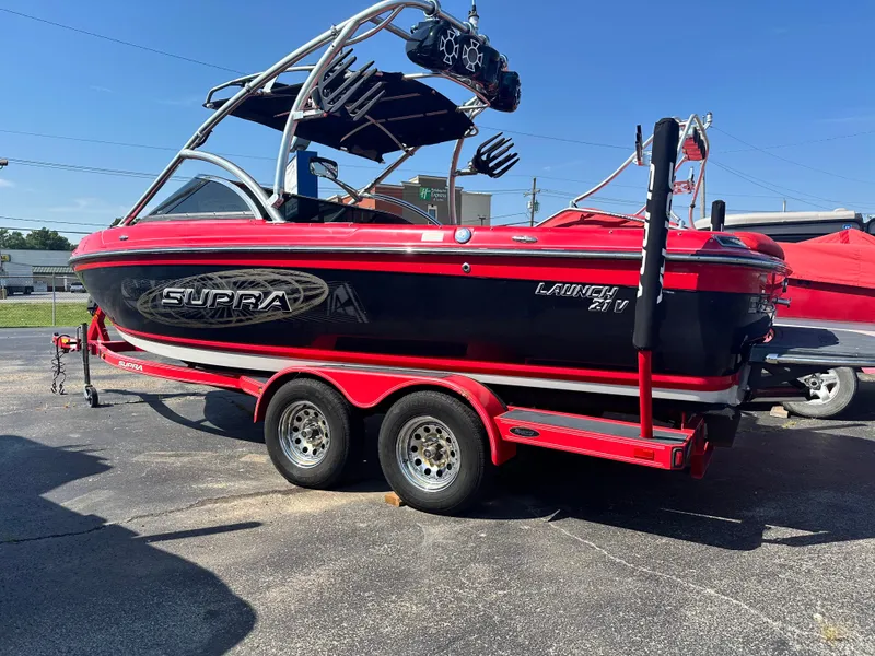 Slide: The Image of 2009 Supra 21V LAUNCH boat on a red trailer in a parking lot. - 2